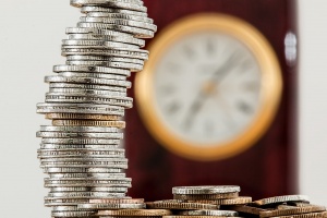 a stack of coins in focus in front of an out-of-focus analog wall clock